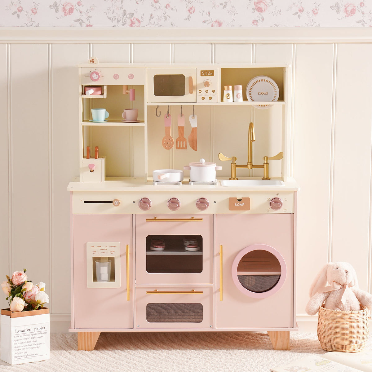 ROBUD Glowwood pink and cream wooden play kitchen with gold hardware, open shelving, oven, and a washer appliance beside it.