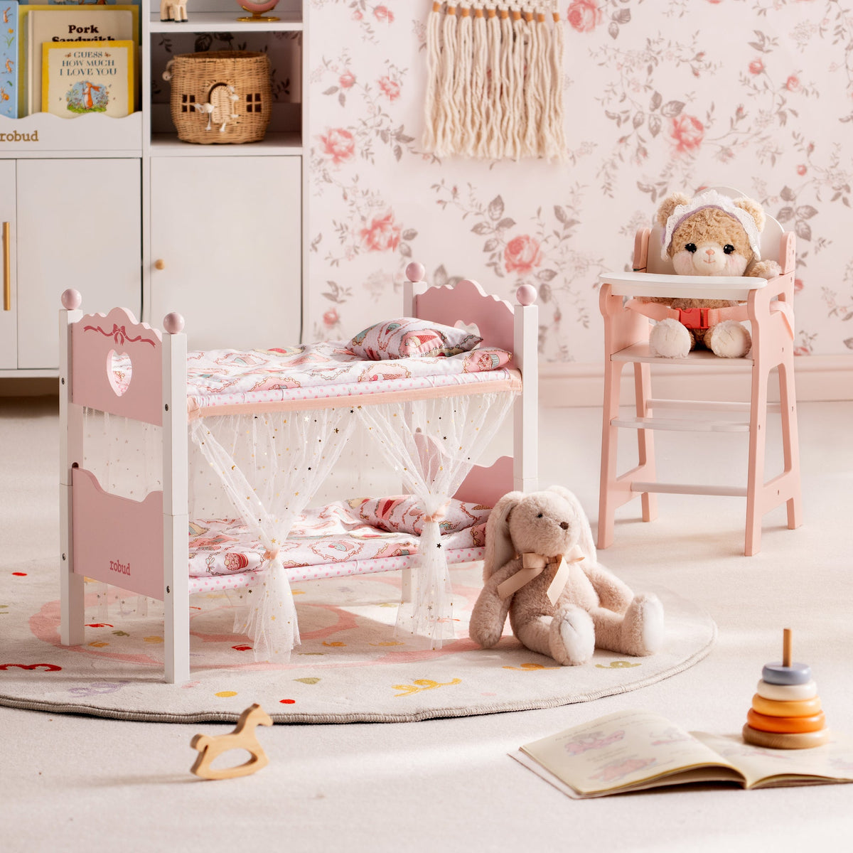 ROBUD white doll bunk bed and pink doll high chair styled in a floral wallpaper nursery with a plush bunny on the rug.