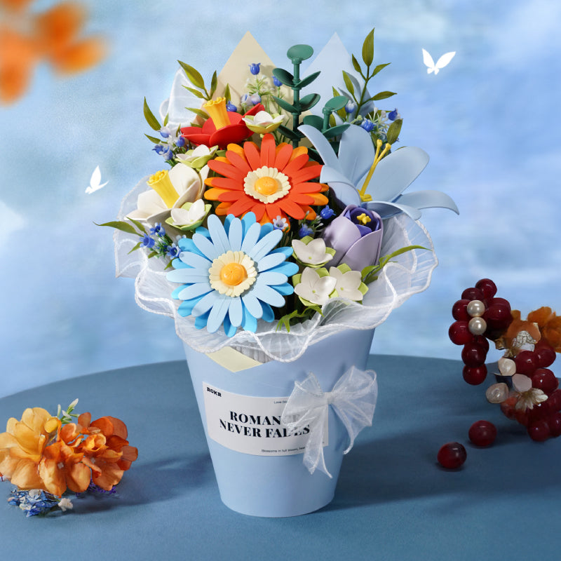 Robotime forever flower bouquet craft kit with orange, blue and white blooms in a white pot beside dried grapes and marigolds