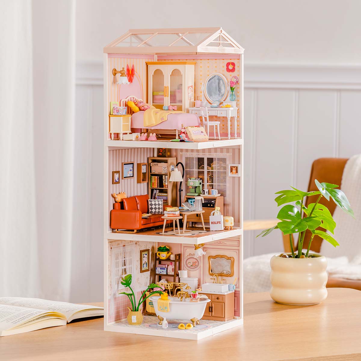 Rolife Super Creator Series 3-in-1 I Shape miniature tower house with three stacked rooms including a pink bedroom, a red orange living room, and a pink floral bathroom displayed on a wooden desk.