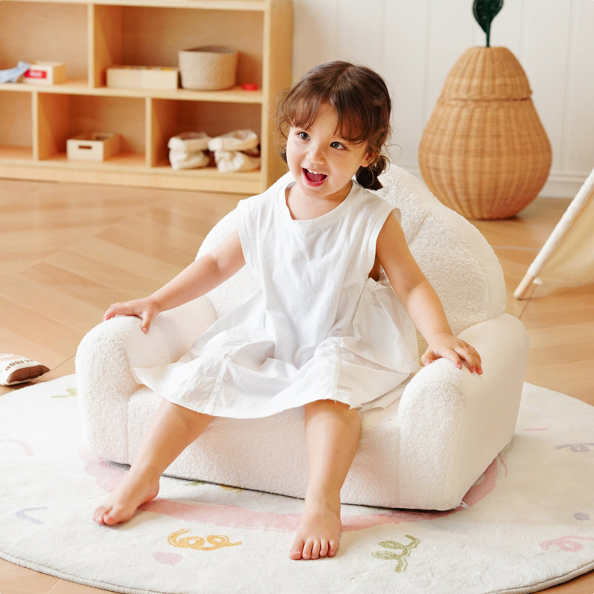 Young girl sitting alone on the ROBUD cream Children's Sofa in a warm Scandi-style playroom with natural light