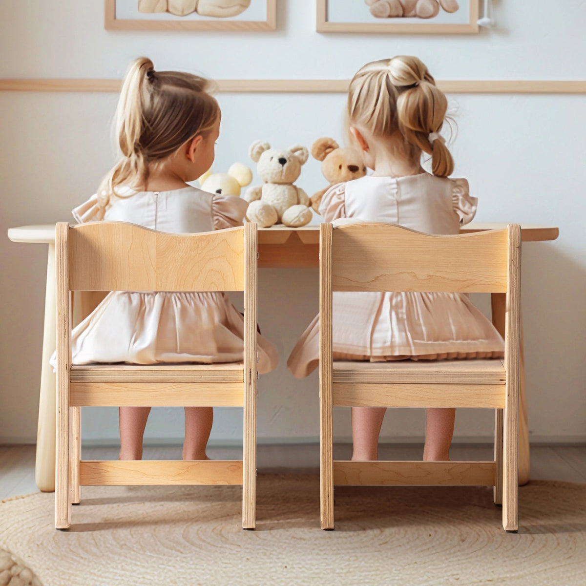 Two girls in matching dresses sitting with their backs to camera at ROBUD natural wood toddler table and chairs with stuffed animals on the table
