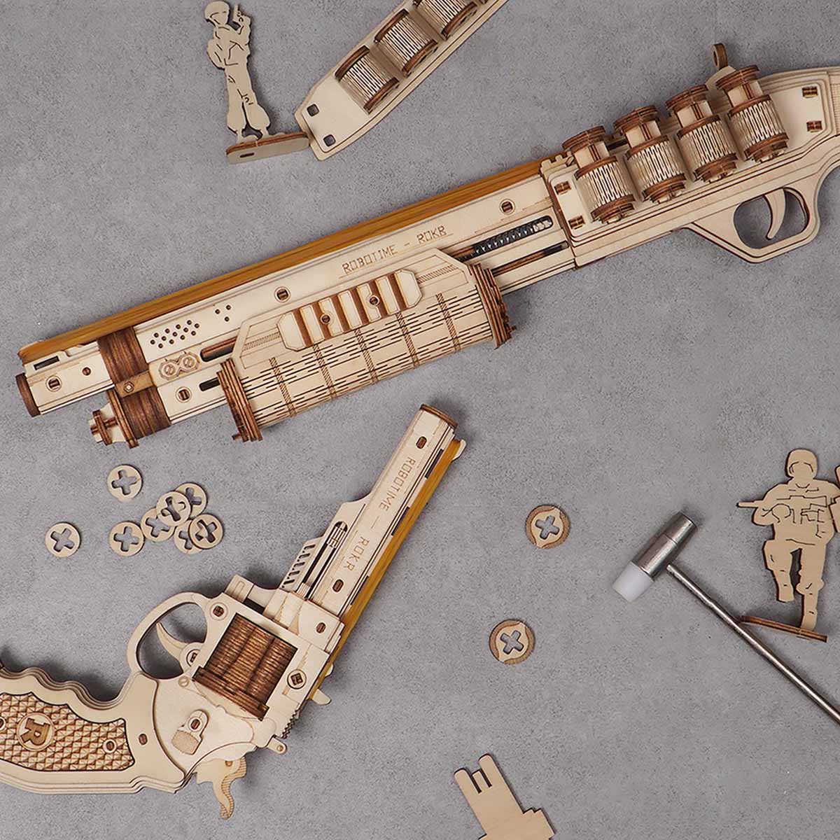 ROKR wooden gun models flat-lay on grey surface with shotgun, revolver and loose gear pieces arranged around them