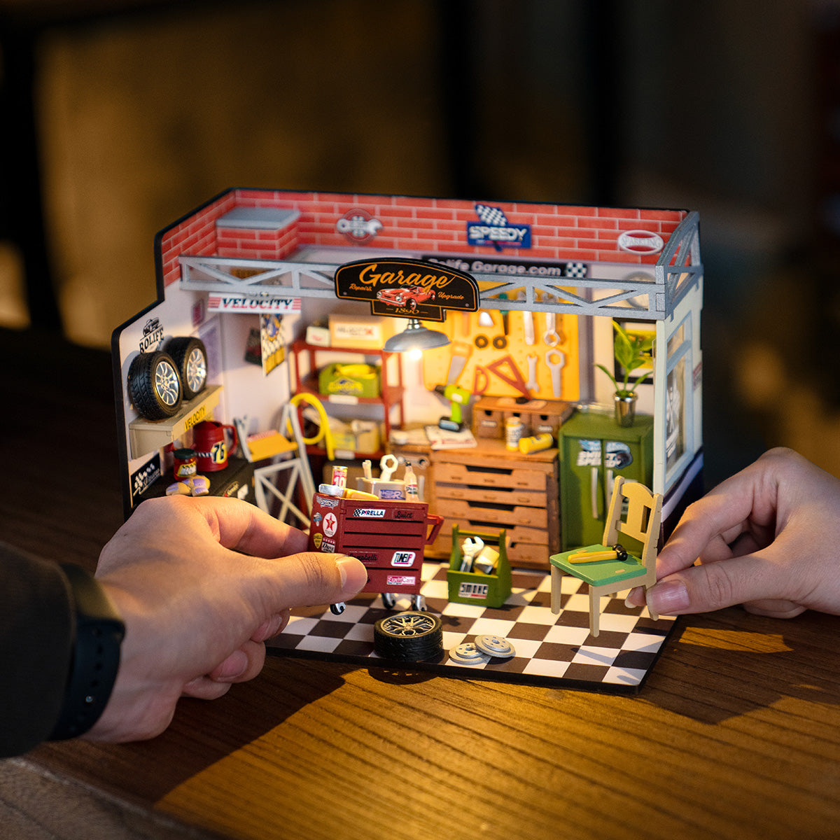 Hands holding a Rolife Garage Workshop miniature scene with car repair details on dark wooden table