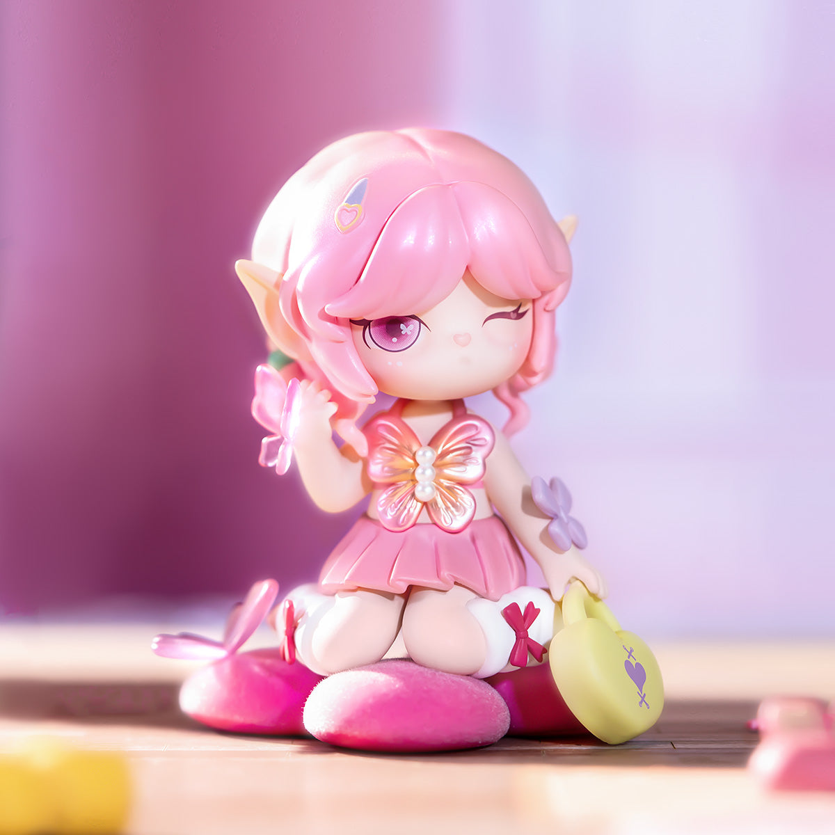 Rolife Suri's Colorful Girls SKXX pink elf figure with pink hair and butterfly brooch sitting on a fluffy pink cushion, holding a small yellow bag on a soft lavender background