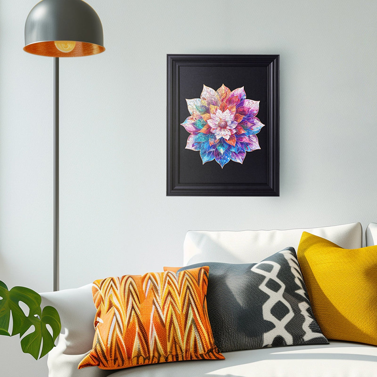 Rowood Mystic Mandala Flower wooden puzzle displayed in a black frame on a living room wall above a sofa with orange and yellow cushions.