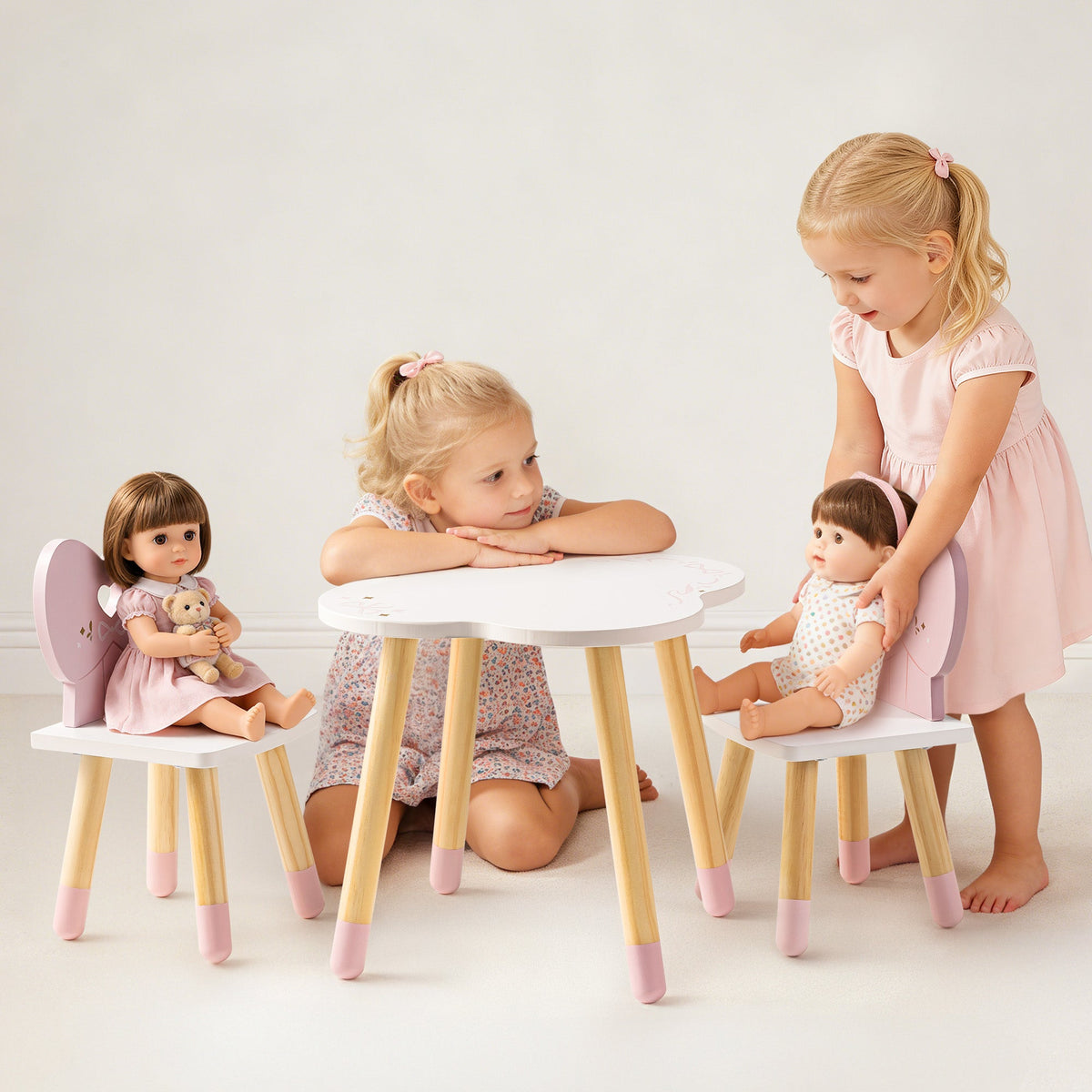 Two girls in pink dresses playing with ROBUD white and pink doll table and chairs set on a clean white studio floor