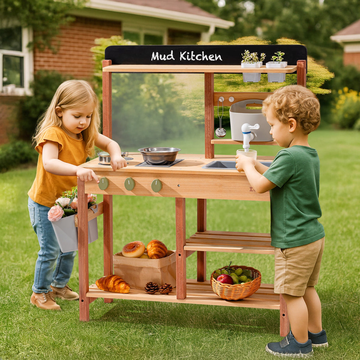 Two children playing together at the ROBUD outdoor wooden mud kitchen in a sunny grass yard, one loading flowers and one operating the water faucet