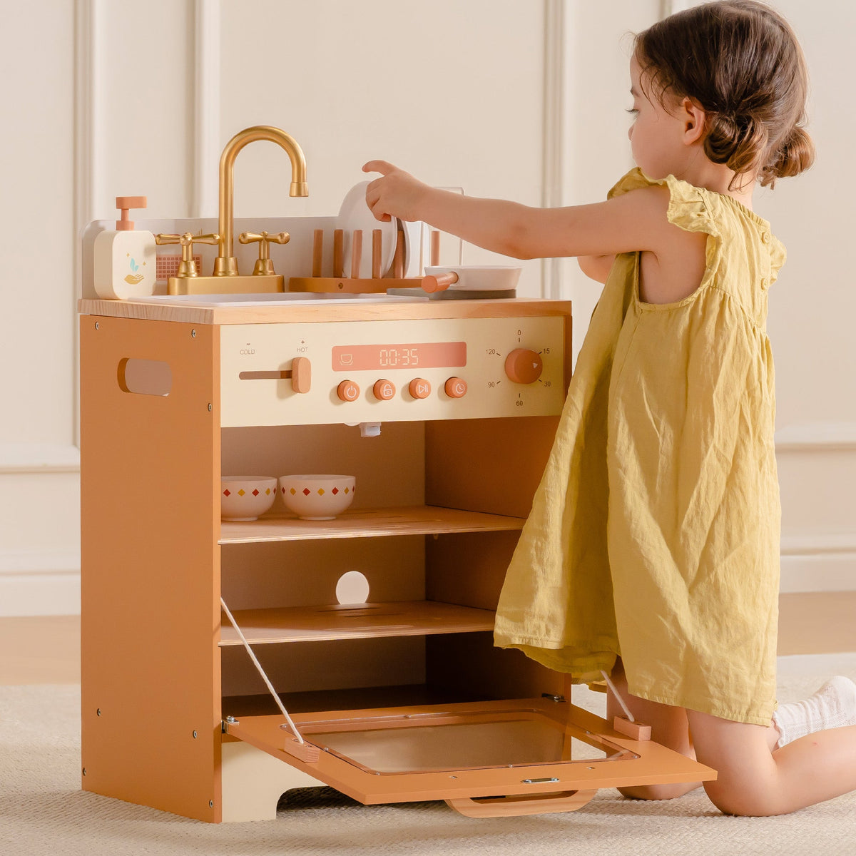 Young girl in yellow dress reaching up to the faucet of ROBUD Wooden Caramel Dishwasher in warm natural wood tones