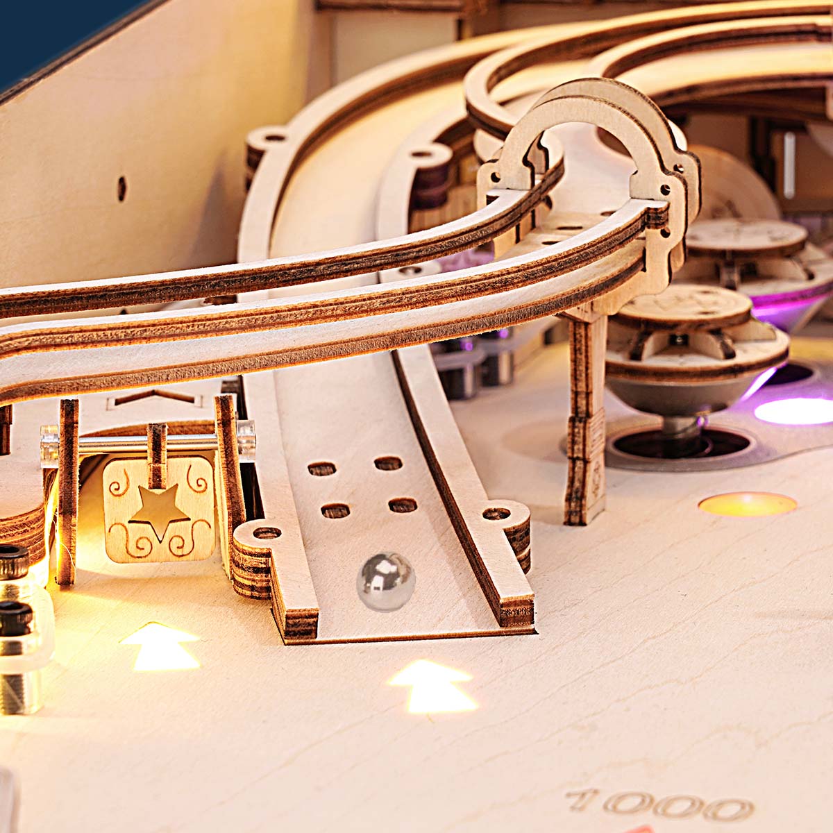 Close-up of the ROKR 3D Pinball Machine wooden puzzle showing the ball launch ramp, curved rail, and lit circular targets on the wooden playing surface