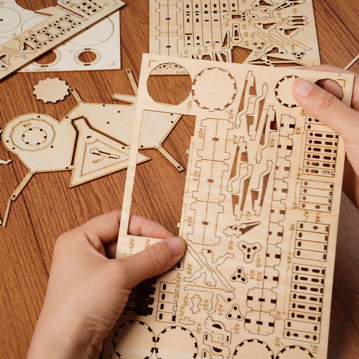 Hands separating laser-cut plywood sheets for Rolife Drum Kit TG409 on a wooden table