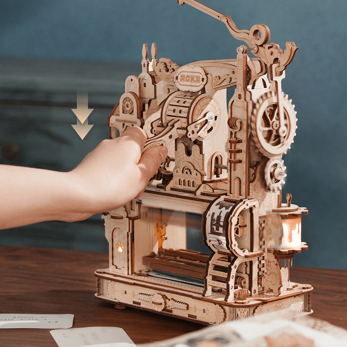 Hand pressing lever on ROKR Classic Printing Press wooden mechanical puzzle with gears and rollers on desk