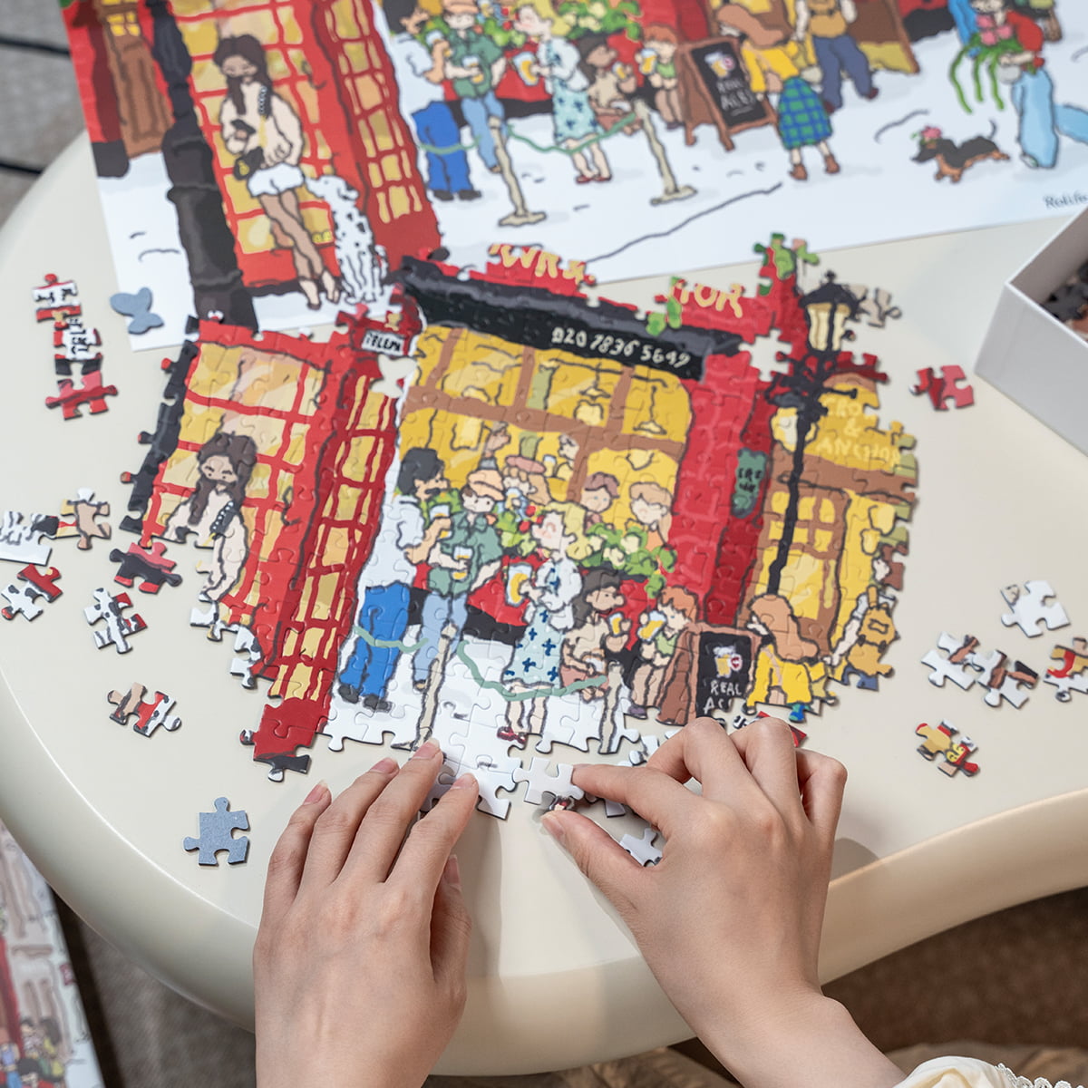 Two people assembling Rolife Welcome to Covent Garden PT006 jigsaw puzzle on a round table with pieces spread around
