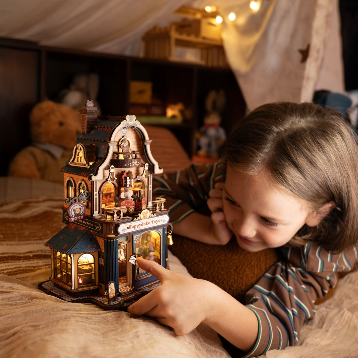 Young girl smiling as she holds an illuminated fantasy miniature house on a wooden table