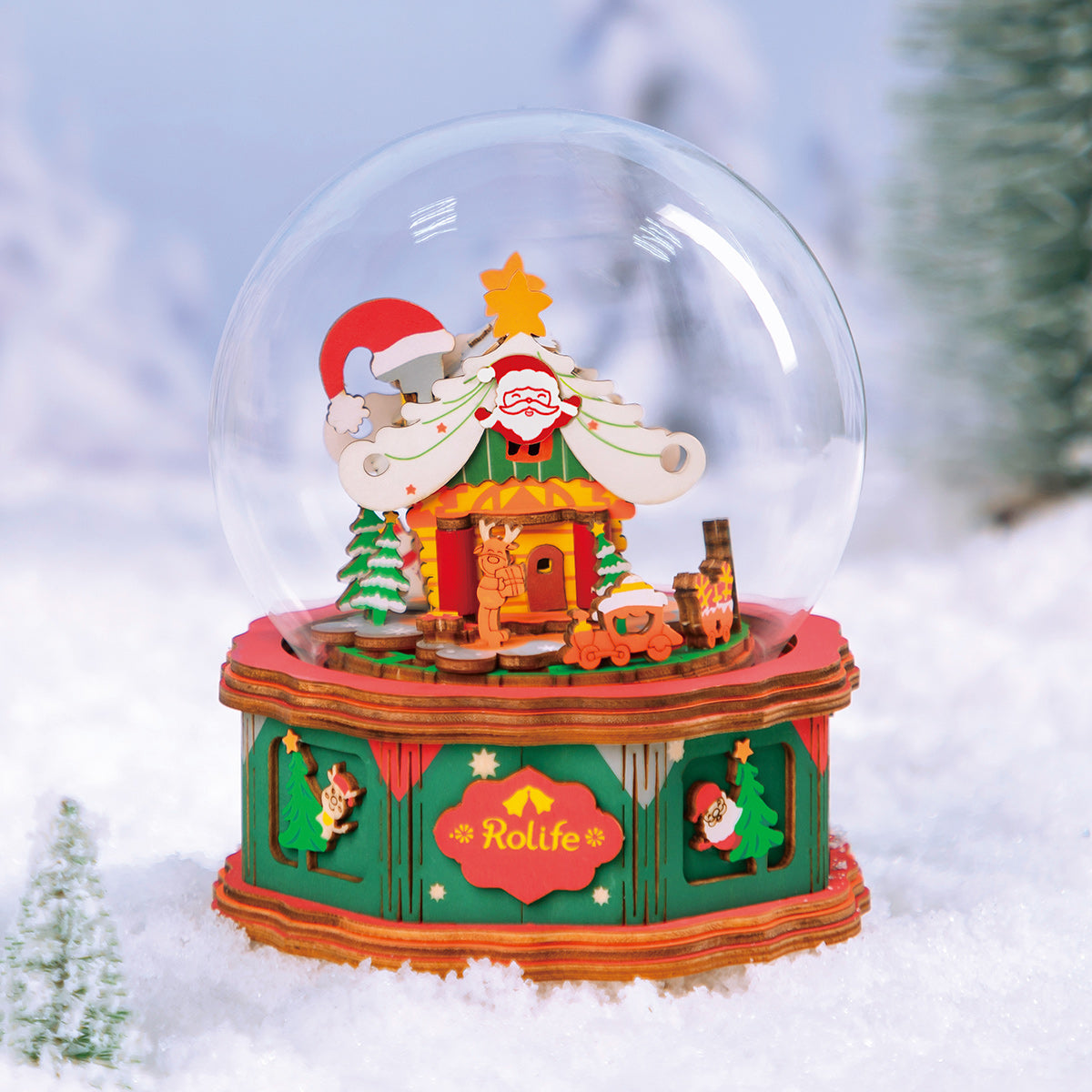 Rolife Christmas town music box standing in soft snow with blue holiday lights behind it.