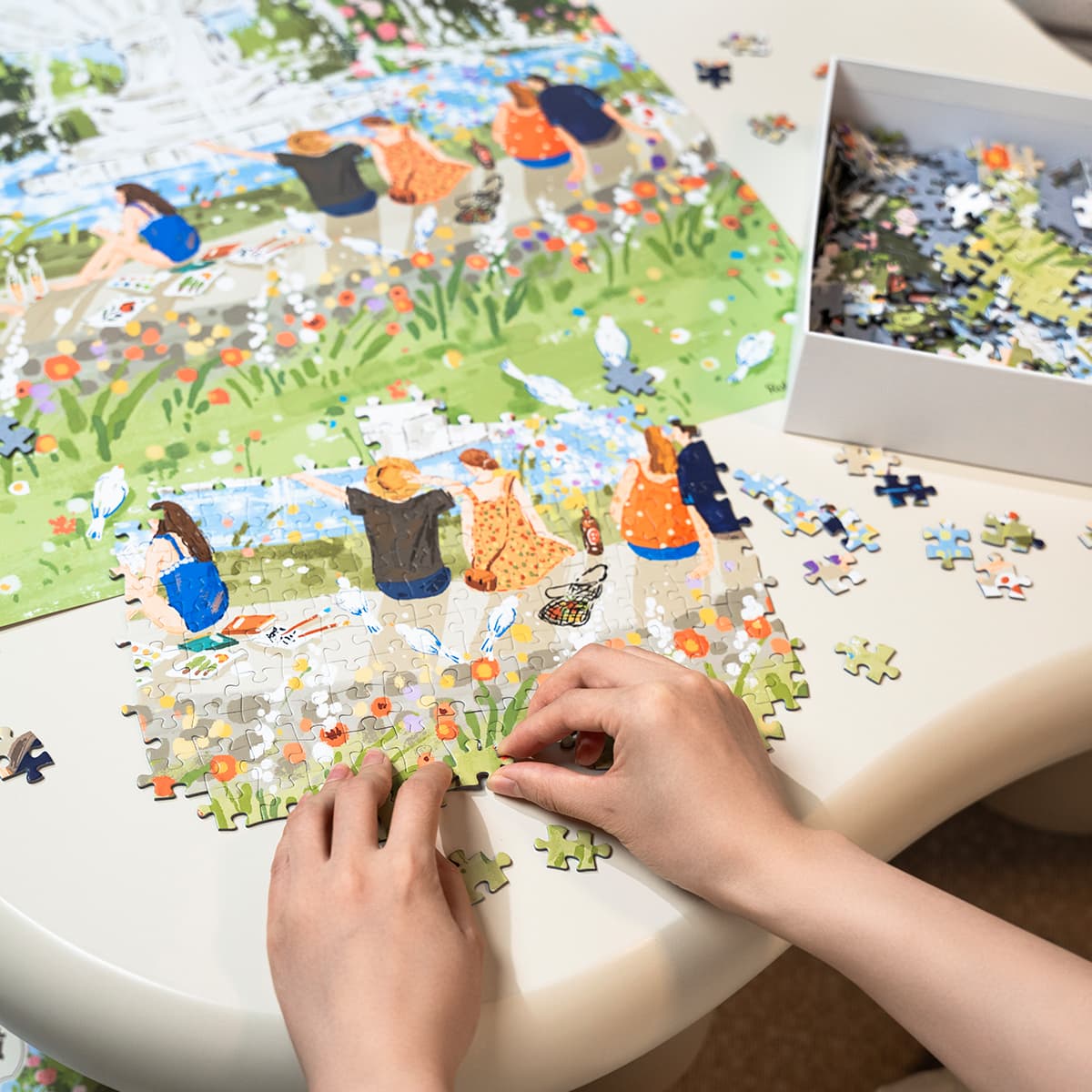 Hands assembling Rolife Afternoon Fountain PT001 jigsaw puzzle on a round table showing illustrated garden fountain scene