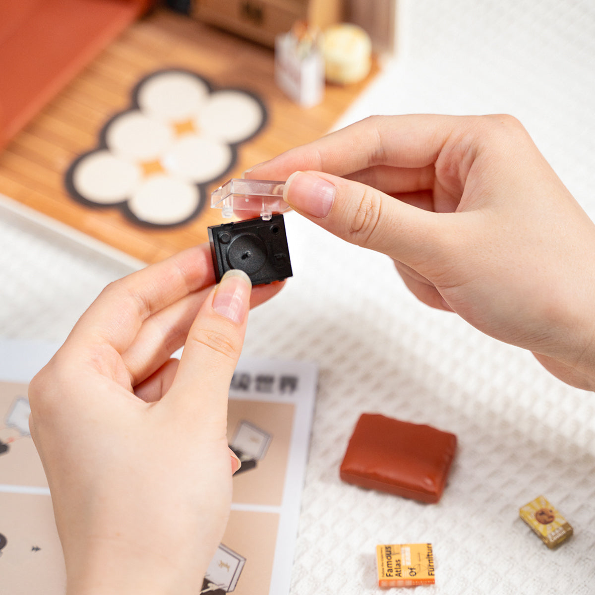 Rolife Cozy Living Lounge DW007 build process showing hands assembling a tiny black electronic component with the
