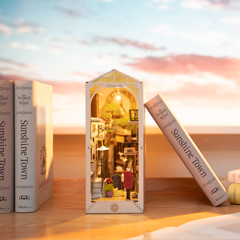 Rolife Sunshine Town book nook standing between matching hardcovers on a wooden shelf with golden sunset sky backdrop