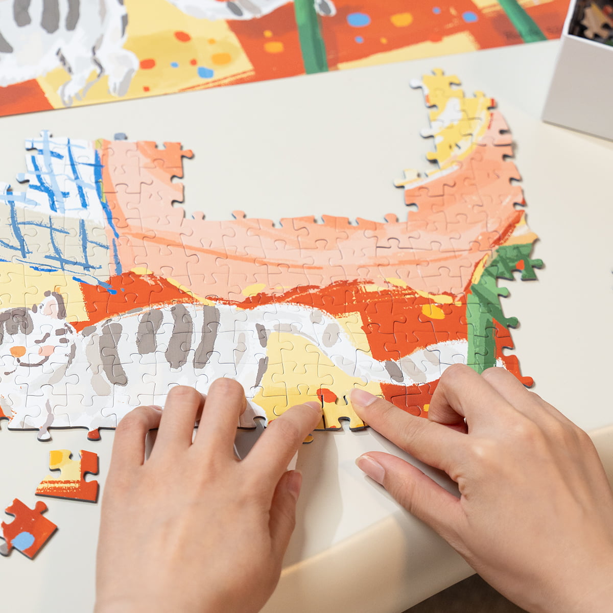 Hands assembling Rolife Leisurely Holiday PT002 jigsaw puzzle on a table showing colorful illustrated picnic scene pieces