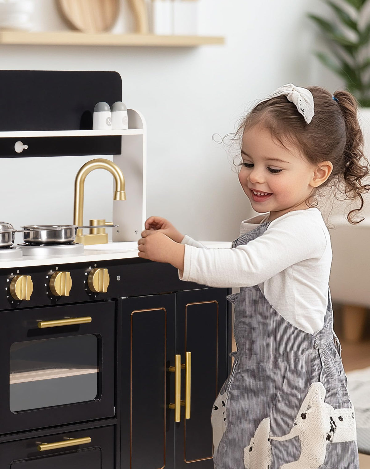 Young girl smiling while playing with ROBUD black and gold wooden kitchen playset in bright white room