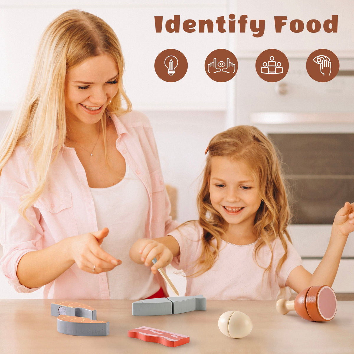 Mother and daughter playing with ROBUD wooden meat cutting playset on a kitchen counter, with salmon, fish, and chicken leg pieces laid out in front