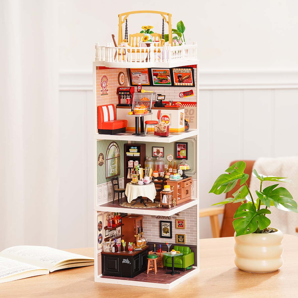 Rolife Super Creator Series 3-in-1 I Shape four-level miniature combining swing rooftop, bathroom, dining room, and garden flower cafe rooms in a white frame on a desk.
