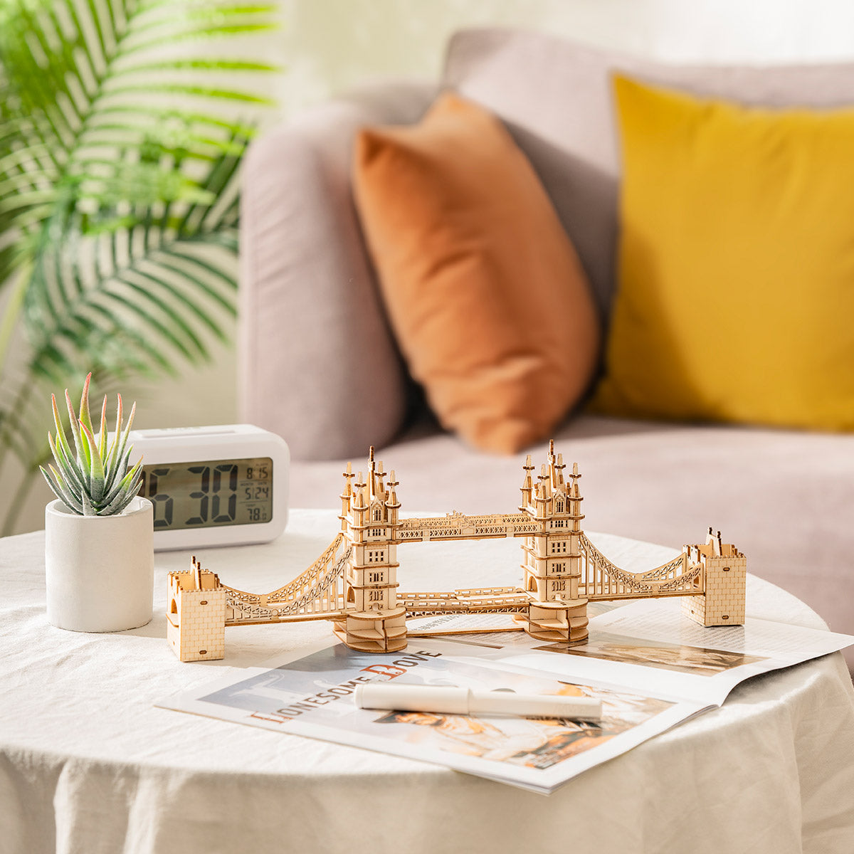 Rolife Tower Bridge wooden puzzle on a marble coffee table beside a clock with a grey sofa and orange cushions behind