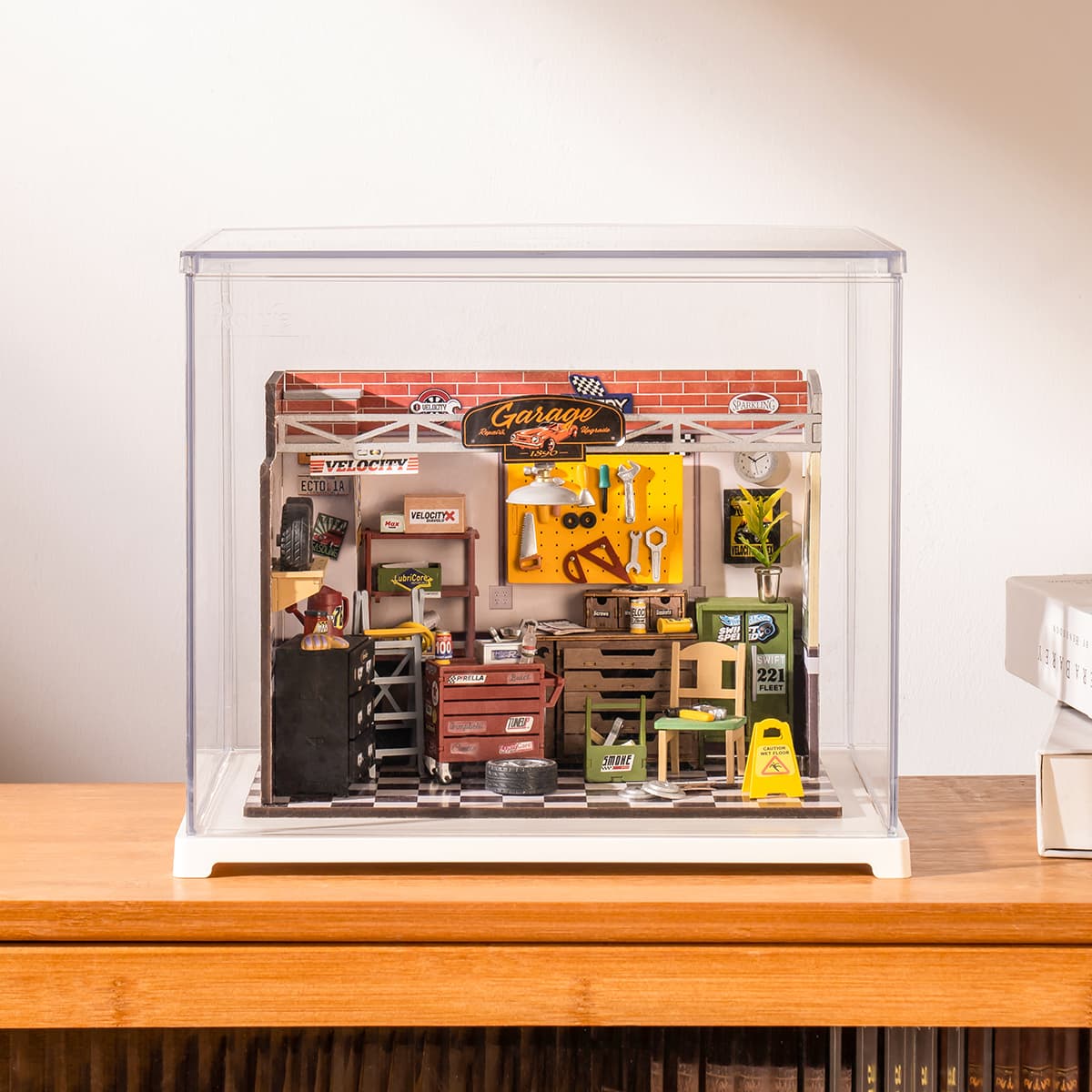 Rolife Garage Workshop miniature sits under a clear case on a warm wooden tabletop.