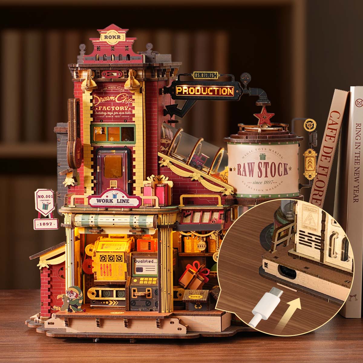 ROKR Dream Gift Factory EAB01 desk lifestyle showing the illuminated factory beside books with a USB charging cable inserted into the wooden base