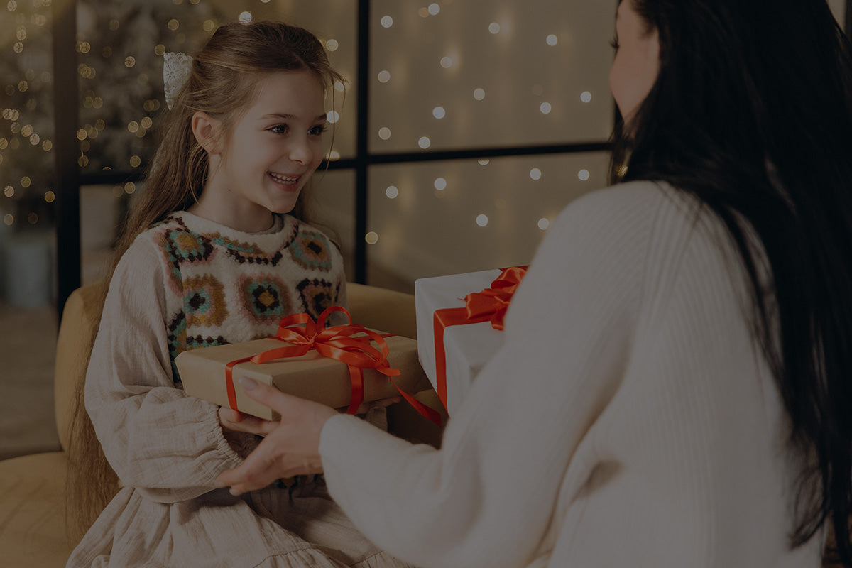 Robotime Online Gifts for Kids photo, mother handing kraft gift boxes to a smiling girl with bokeh holiday lights