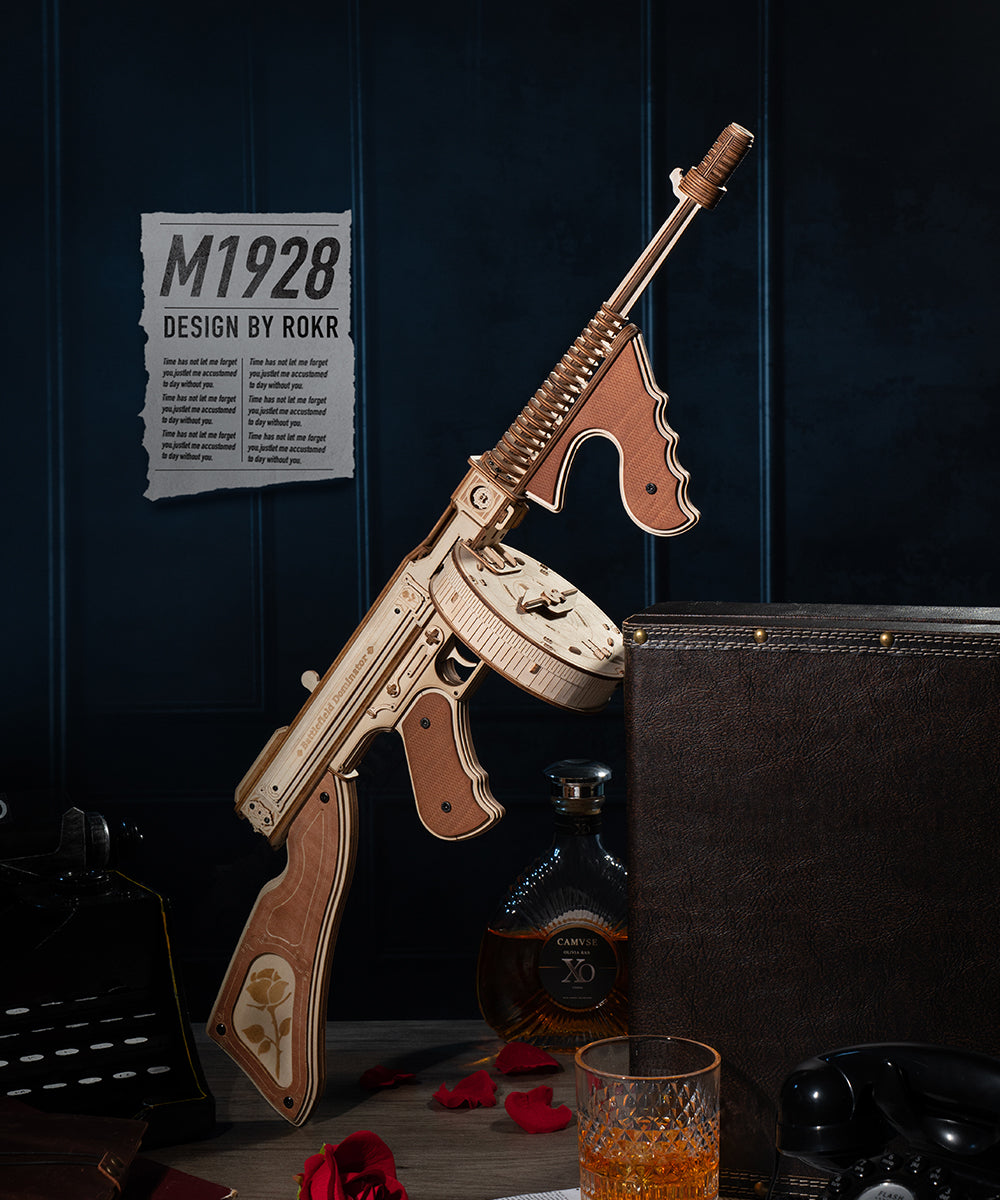 ROKR Thompson Submachine Gun wooden model kit LQB01 fully assembled standing upright in a dark blue moody setting with M1928 design label and whiskey glass beside it