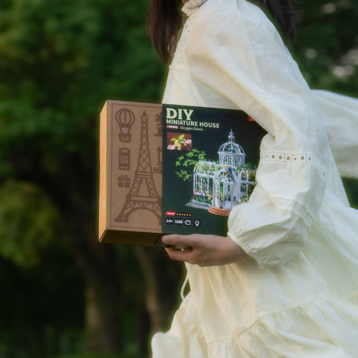 Woman in a white dress carrying the Rolife Oxygen Oasis greenhouse kit box outdoors