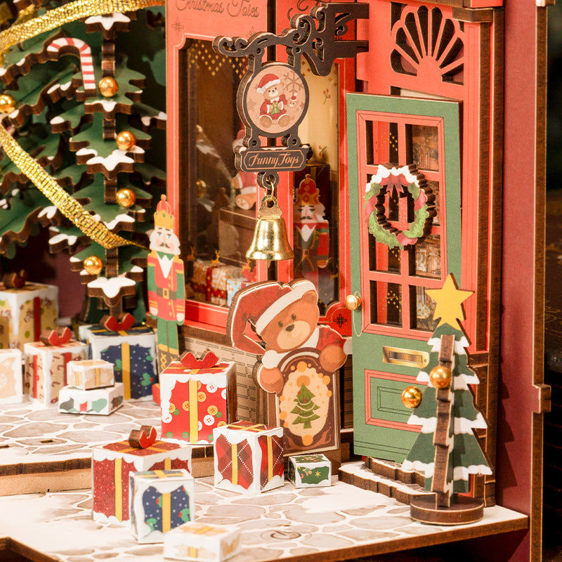 Close-up of Rolife Christmas Teddy Playhouse book nook facade showing a gold bell, teddy bear figure, gift boxes and a decorated Christmas tree.