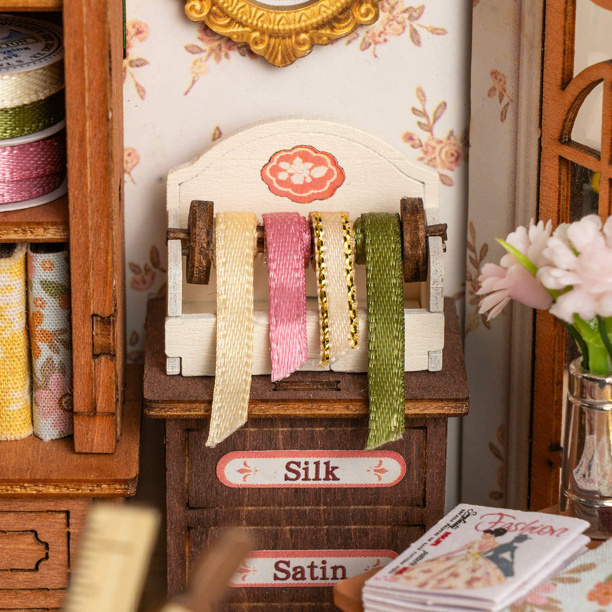 Rolife Elsa's Tailoring DG178 close-up of the miniature wooden ribbon rack holding yellow, pink and green silk ribbons labeled Silk and Satin