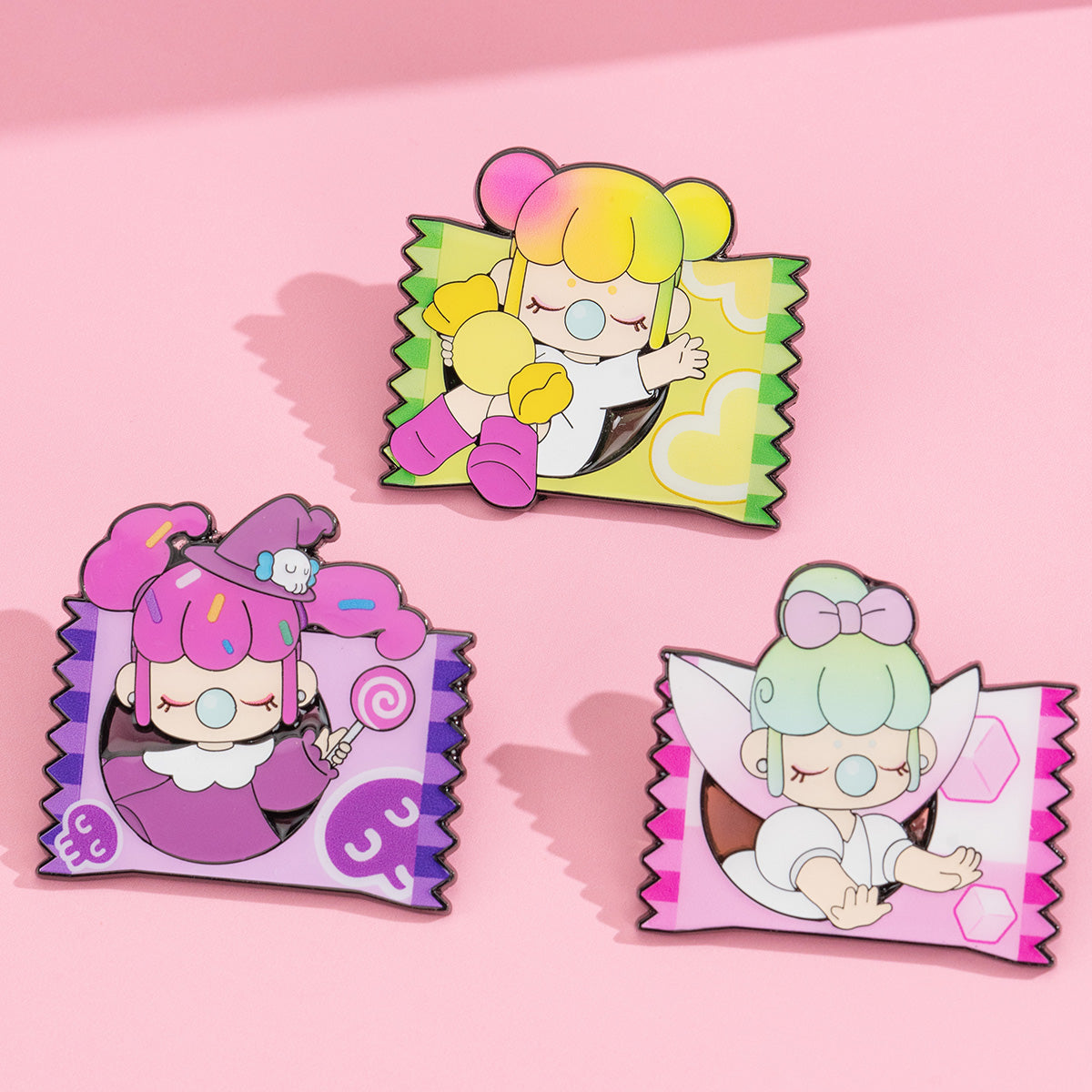 Three Rolife Nanci Sweet Time candy-wrapper enamel pins arranged on a pink surface featuring the Gift Bag, Witch, and Tea Cup designs in yellow, purple, and pink tones