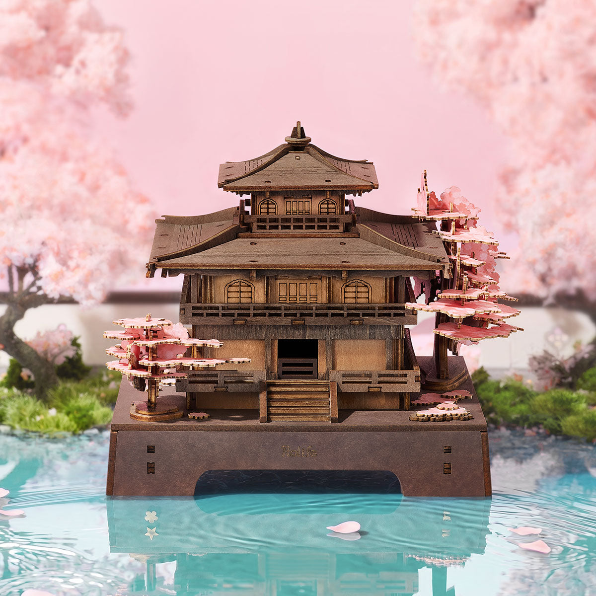 Rolife Sakura Pavilion TGA07 3D wooden puzzle hero shot showing the multi-tiered pagoda on a pink reflective base surrounded by cherry blossom petals