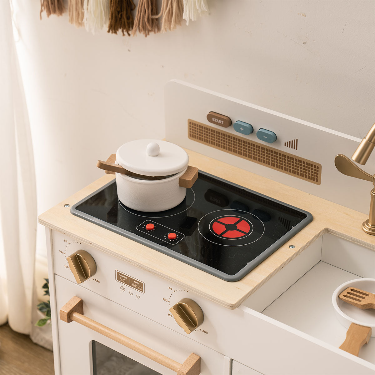 ROBUD white Montessori kitchen close-up of black induction stovetop with pot and wooden utensils.