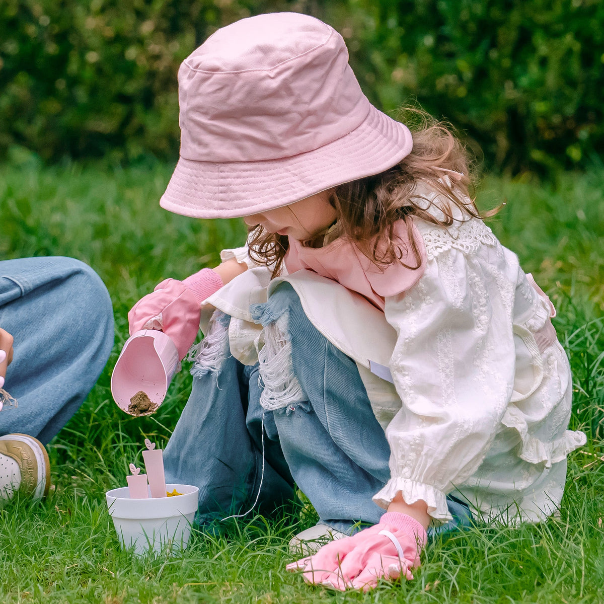 ROBUD Kids Gardening Set pink series spread on green meadow with apron, hat, watering can, tools and accessories among colorful wildflowers