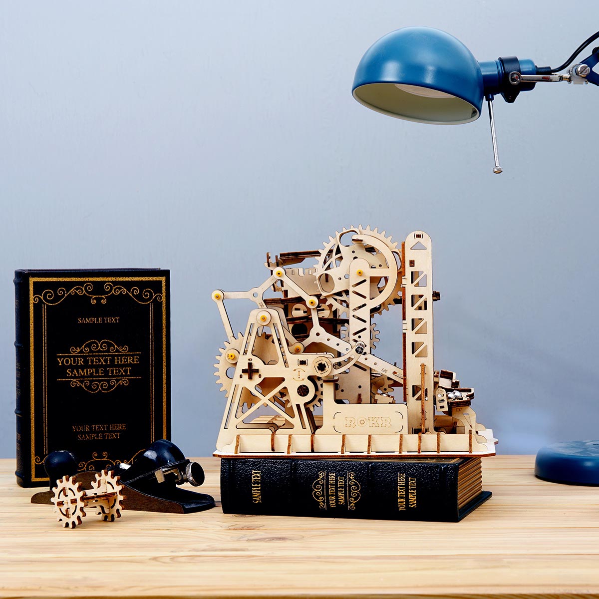 ROKR Marble Climber Fortress LG504: Nahaufnahme des Zahnradturms auf einem Holzschreibtisch neben einer blauen Schreibtischlampe und Büchern