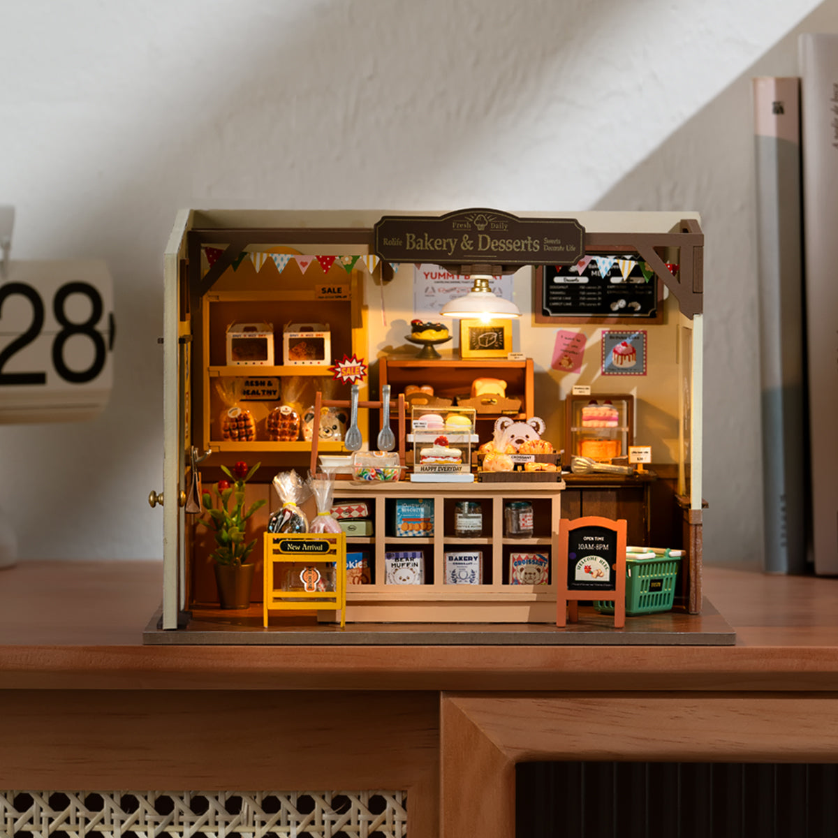 Flat-lay of the Rolife Becka's Baking House DG161 miniature kit components spread across a warm wooden surface, including tiny furniture, food replicas, and structural frame pieces.