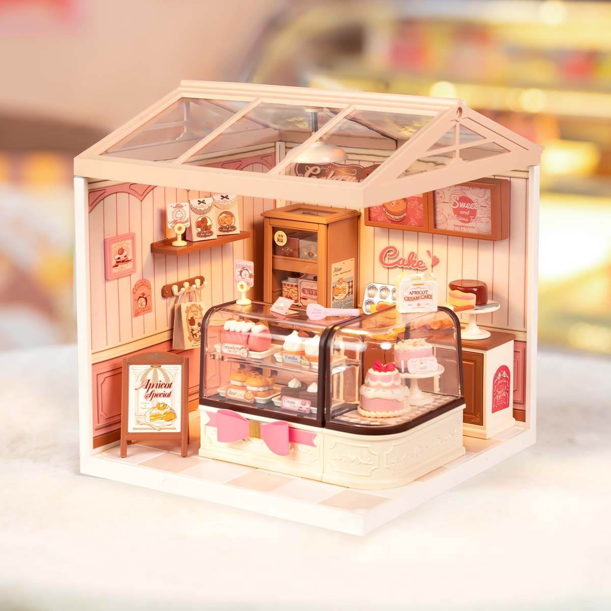 Rolife Tasty Cake Shop DIY miniature house DW019B lifestyle scene with the completed single-room bakery module featuring cake display counter, apricot special signboard, and soft interior lighting.