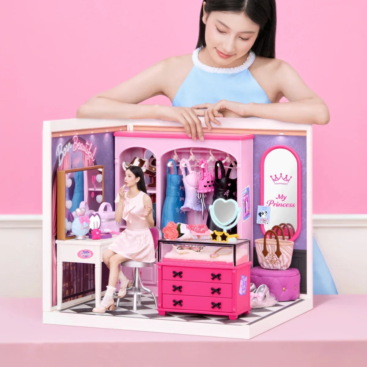 Miniatur-Ankleidezimmer mit Schminktisch, Kleiderstange und rosa Schubladen; eine Person beugt sich vor rosa Hintergrund über das Modell.