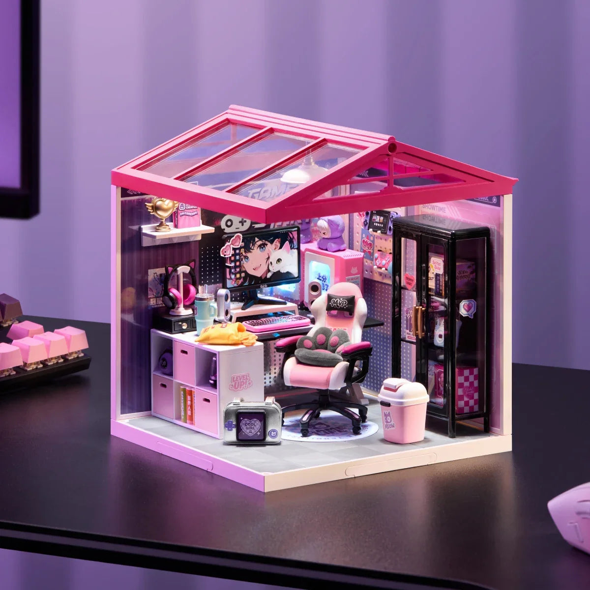 Miniatur-Gaming-Zimmer mit rosa Dach und transparenten Paneelen auf einem dunklen Schreibtisch; sichtbar sind Gaming-Stuhl, Schreibtisch, Monitor und Schrank.