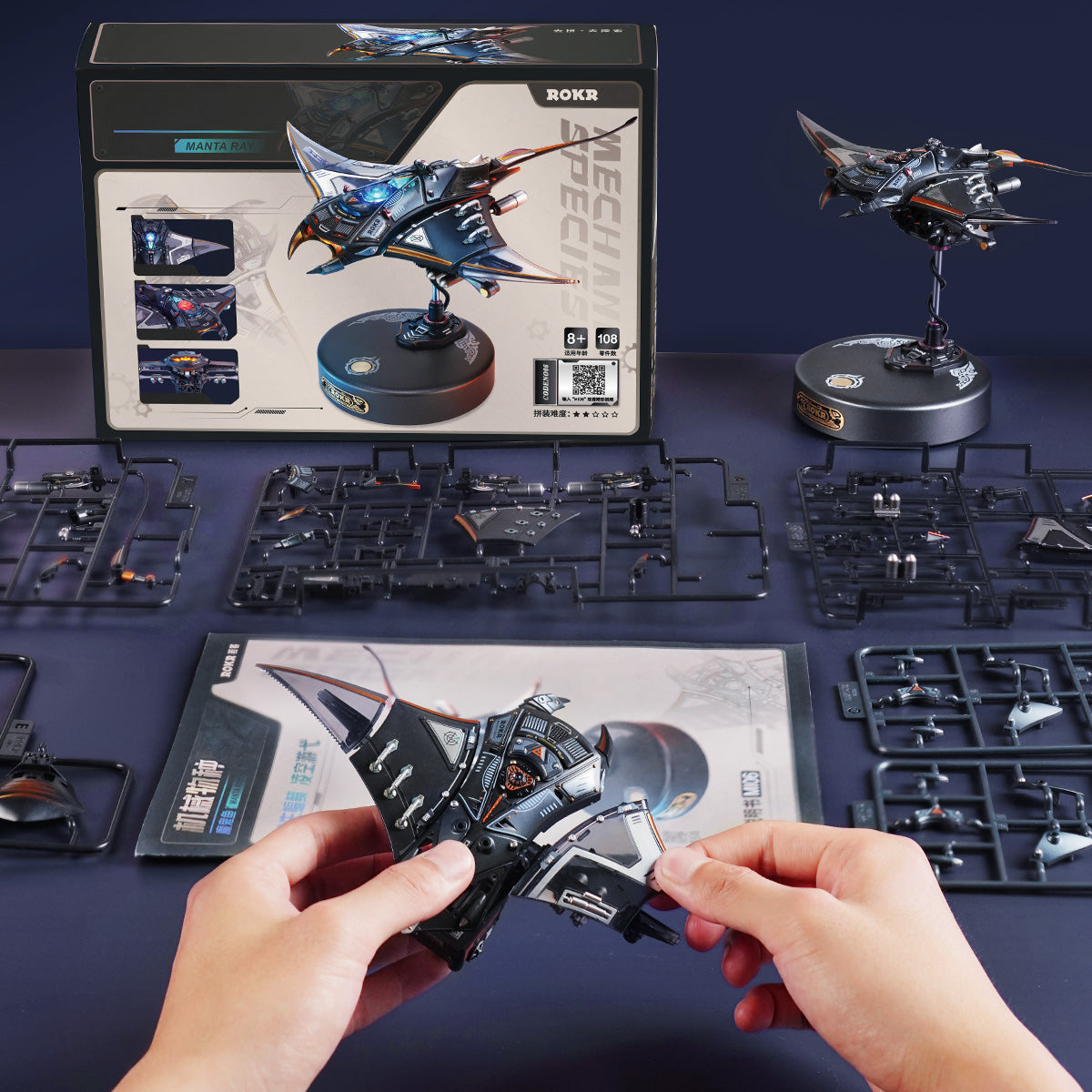 ROKR Manta Ray MI06 mechanical puzzle box and completed dark blue model on its stand displayed with unassembled runners and instruction booklet on a table