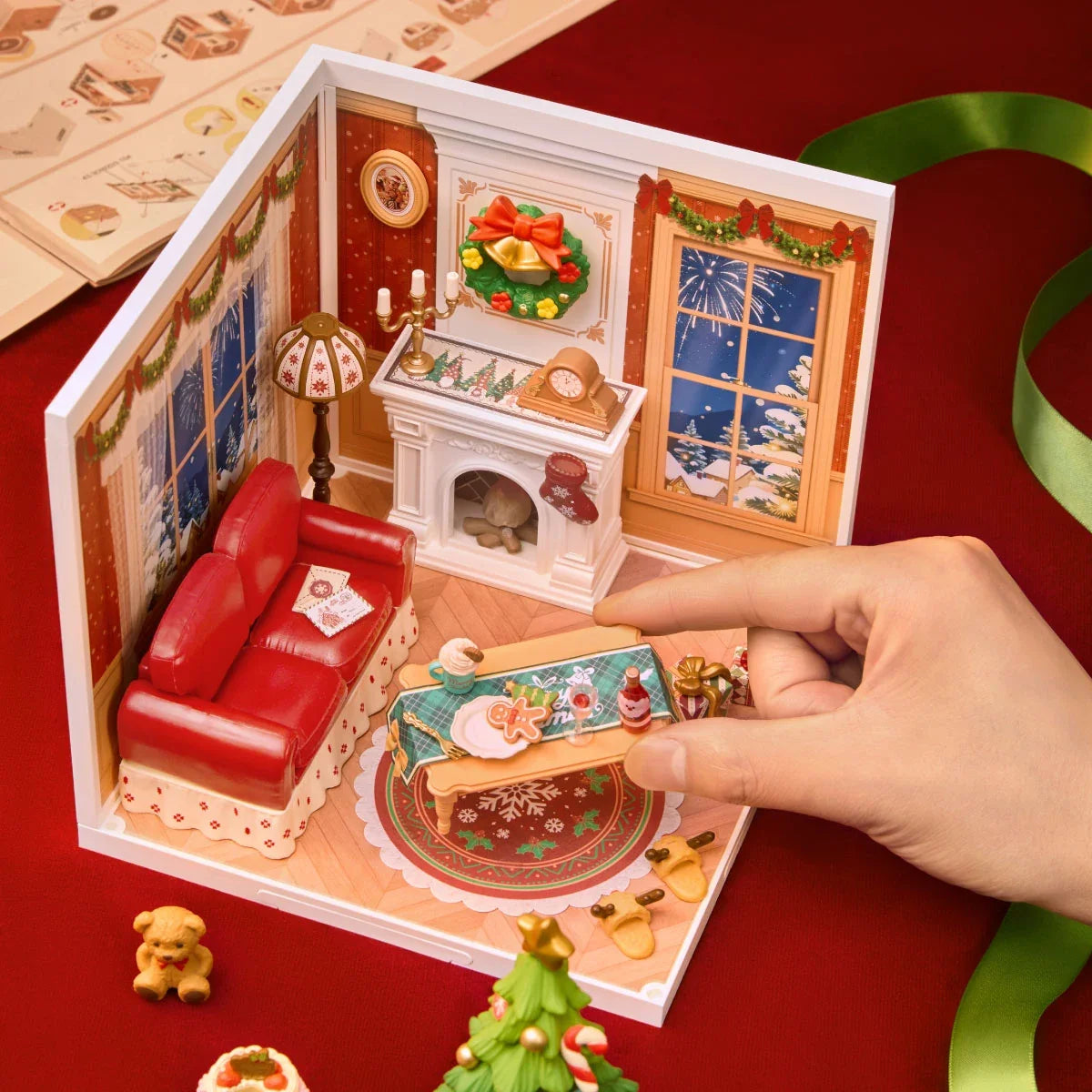 Eine Hand stellt eine Miniaturflasche auf den Tisch im Rolife-Weihnachtswohnzimmer-Diorama; daneben liegen Anleitung und lose Teile.