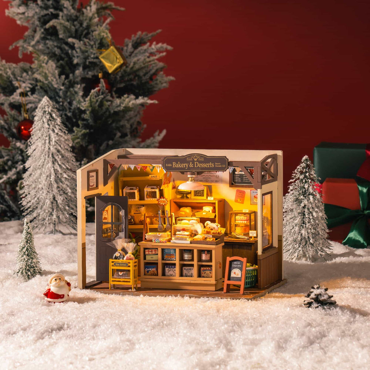 Rolife Beckas Baking House miniature DG161 shown outdoors in snow beside Christmas tree with warm glowing light