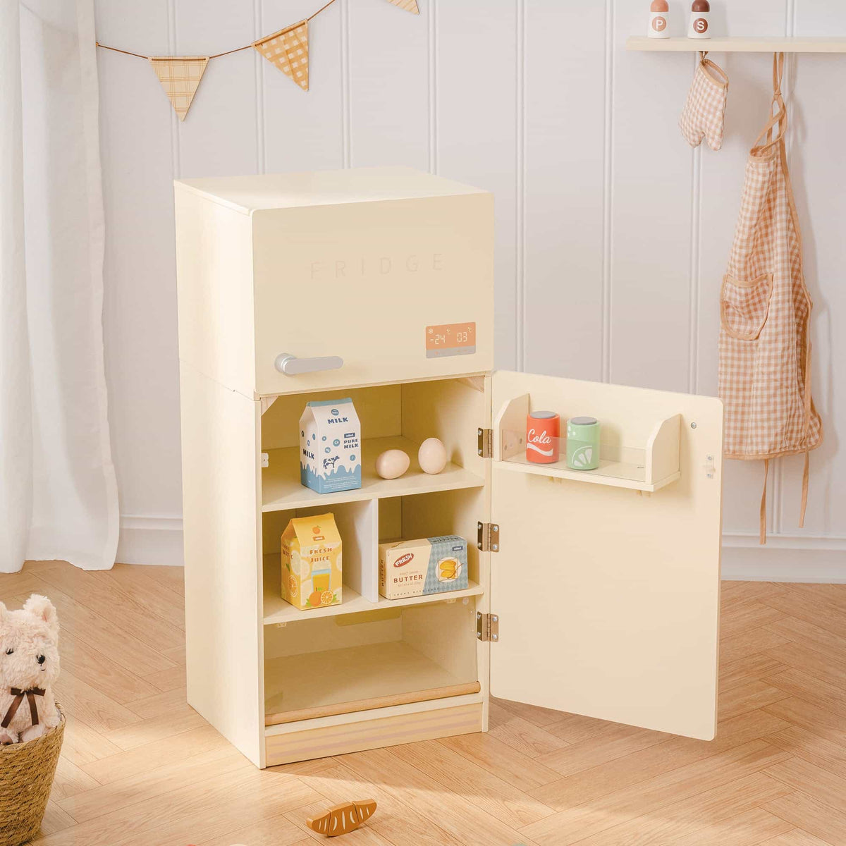 ROBUD creamy wooden play fridge in a styled playroom with door open showing milk cartons, eggs, juice, butter, and cola cans on shelves and door rack