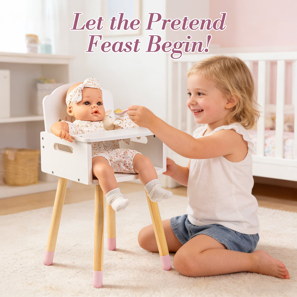 Toddler girl feeds her baby doll seated in the ROBUD white wooden high chair on a playroom floor.