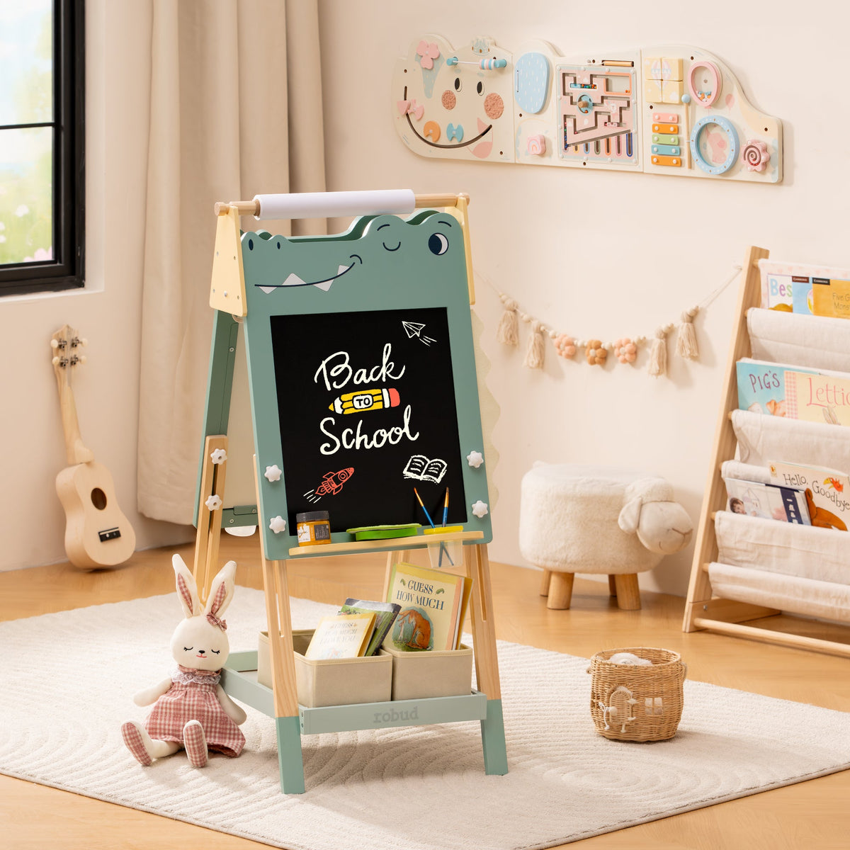 ROBUD dinosaur art easel with chalkboard side facing out shown in a light playroom with bookshelf in the background.
