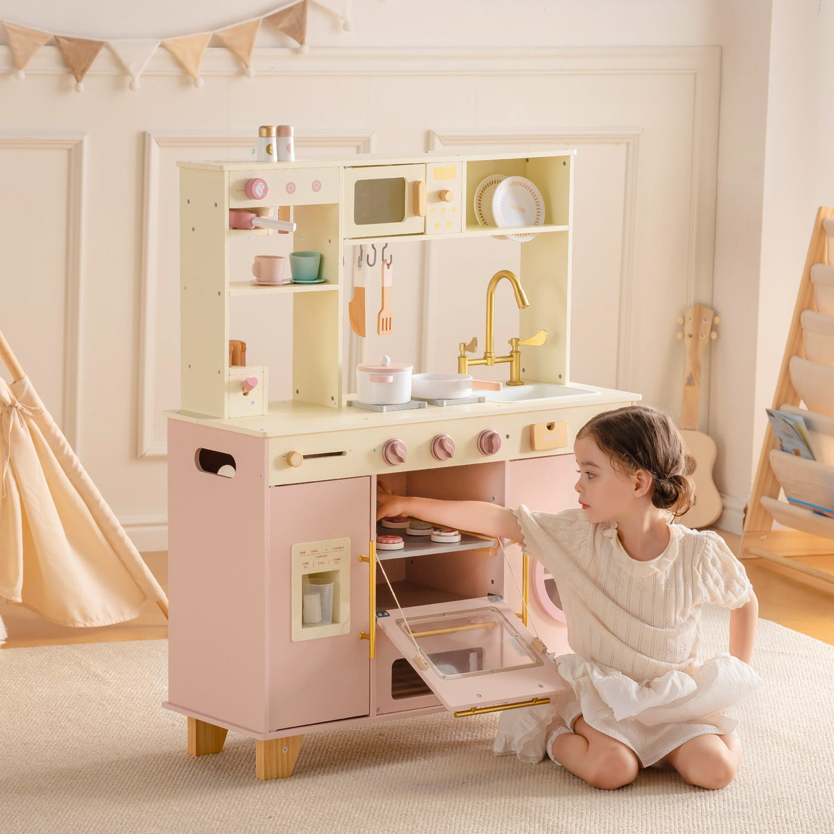 ROBUD Pink Baking Kitchen lifestyle view with young girl sitting beside the full-size pink wooden play kitchen in cozy room setting